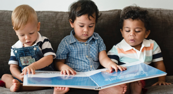 Three toddlers sitting on a couch all looking at the same children's book.