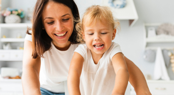 Adult female and toddler in a bright at home setting smiling.