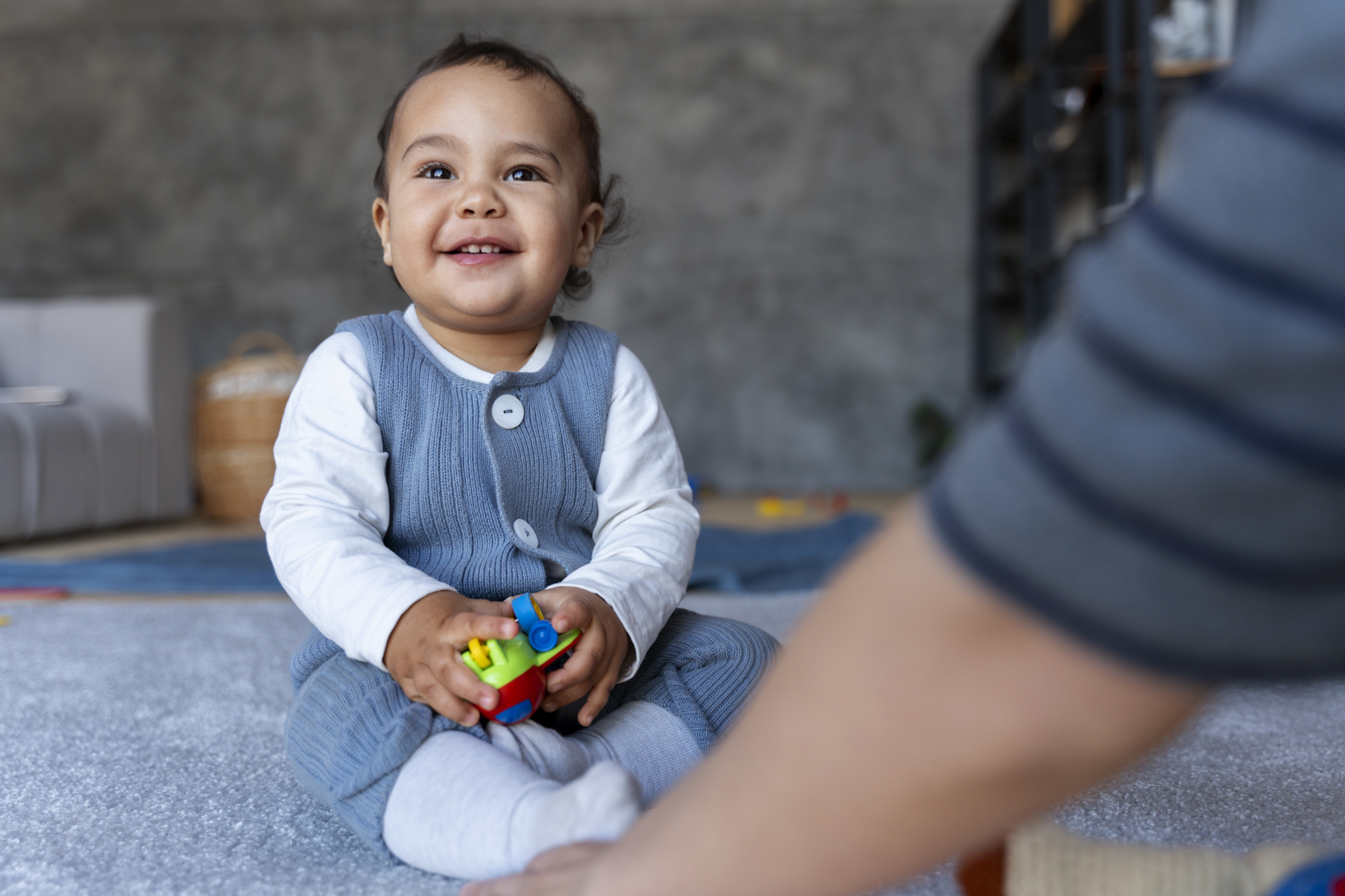 Smiling Baby Playing With Toy while sitting on the comfy carpet floor.