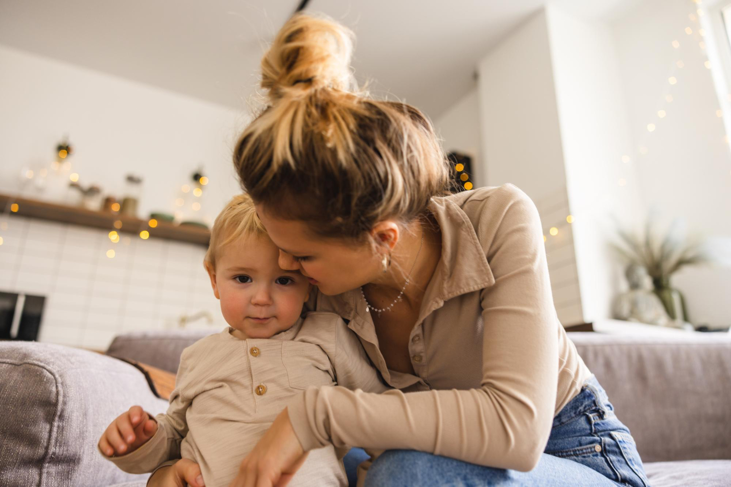 Adult female and little toddler sitting on couch while she kisses the toddlers cheek. 