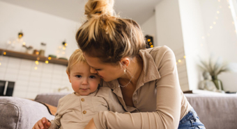 Adult female and little toddler sitting on couch while she kisses the toddlers cheek. 