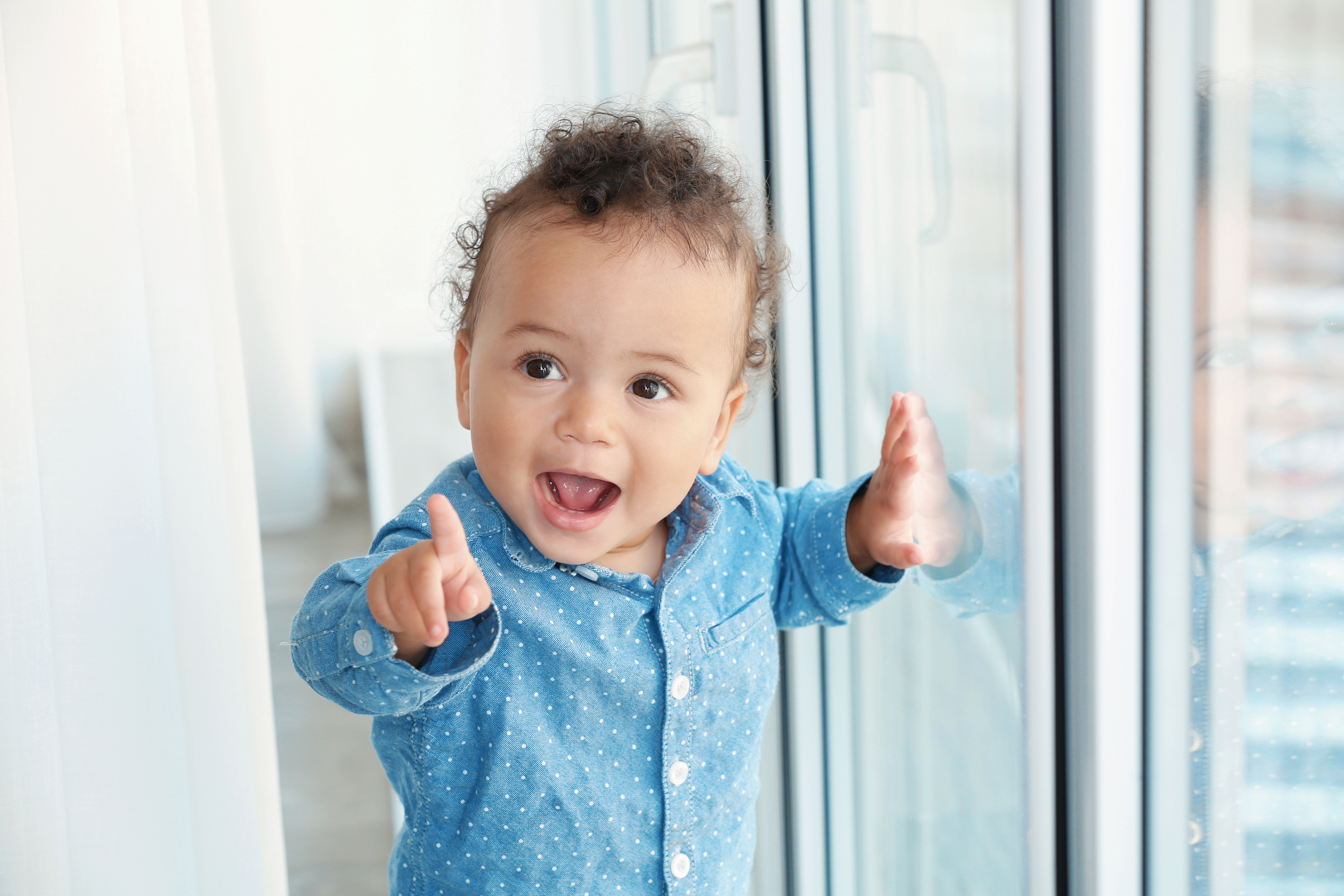 Cute young toddler wearing blue button up denim shirt points into the distance  with big smile on face. 