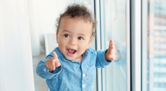 Cute young toddler wearing blue button up denim shirt points into the distance  with big smile on face. 