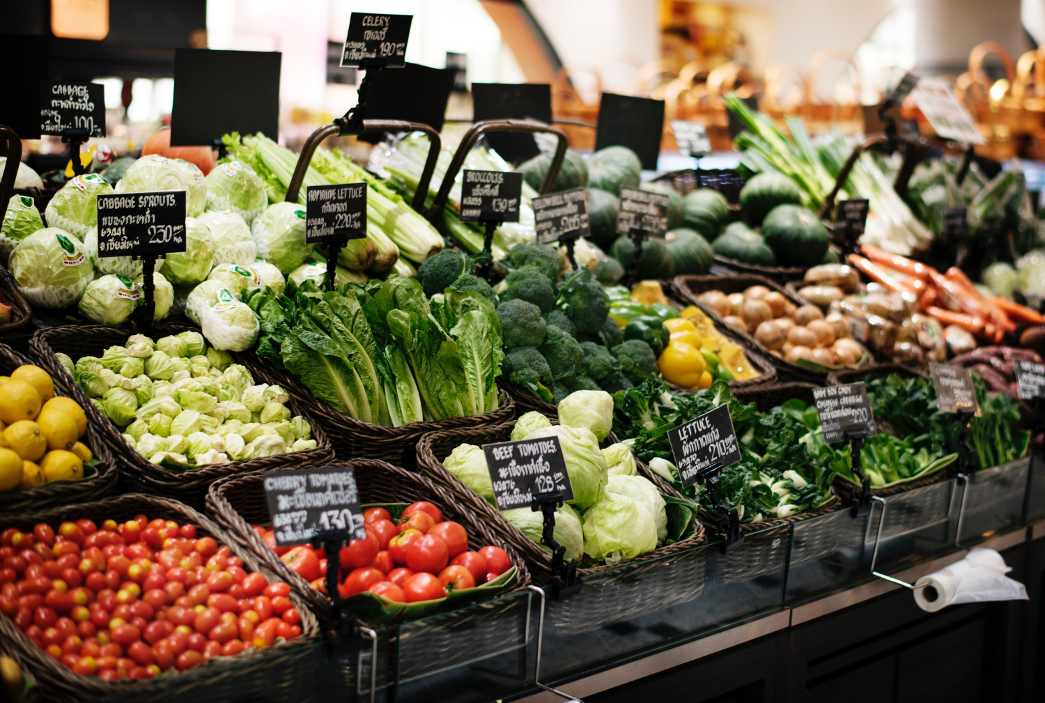 Grocery store produce isle, multiple vegetables shown in bins. Tomatoes, lettuce, cabbage, carrots and more. 