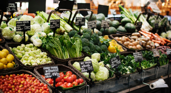 Grocery store produce isle, multiple vegetables shown in bins. Tomatoes, lettuce, cabbage, carrots and more. 