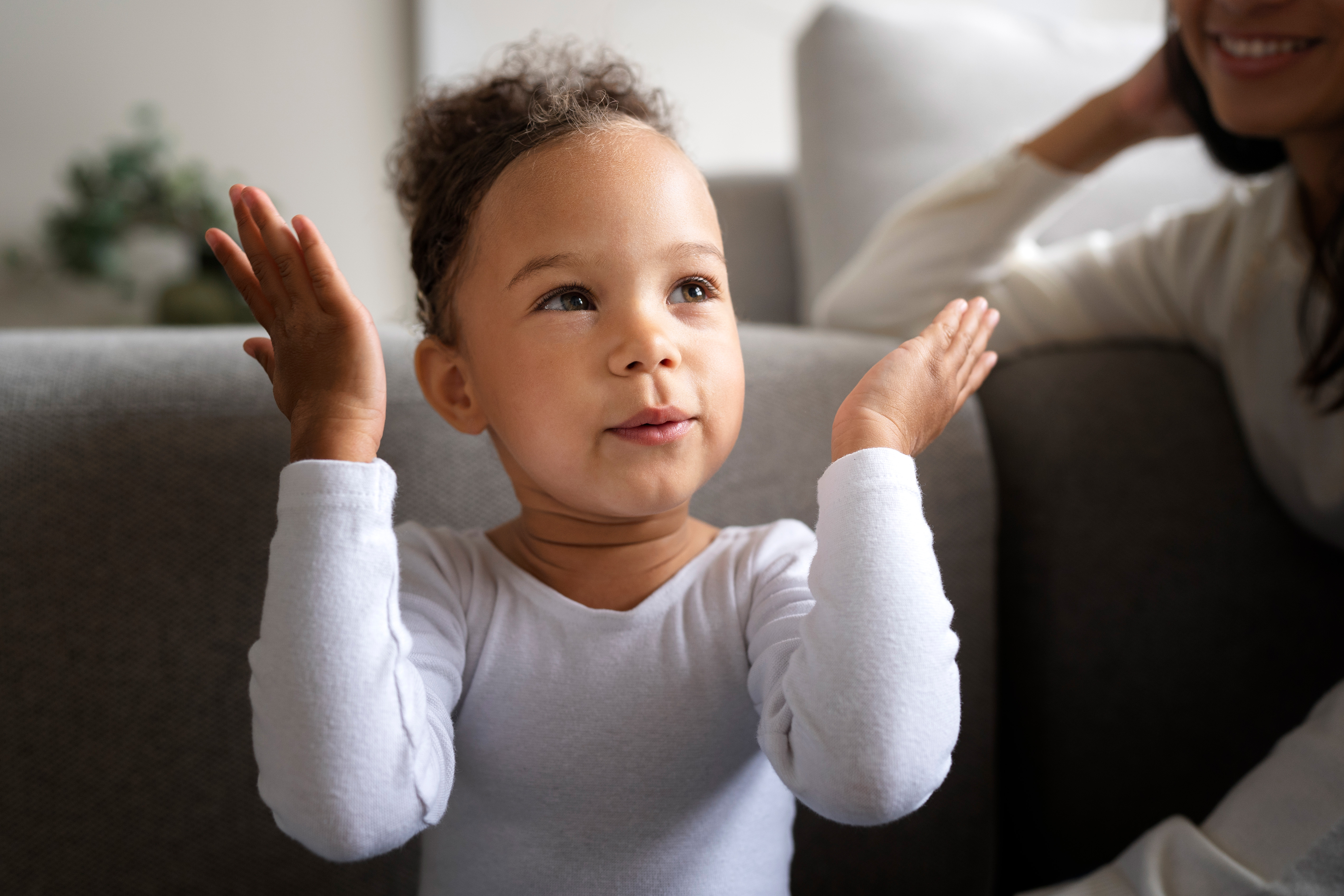 Closeup of toddler girl holding her two hands up by her head, smiling. 