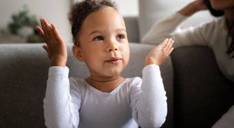 Closeup of toddler girl holding her two hands up by her head, smiling. 