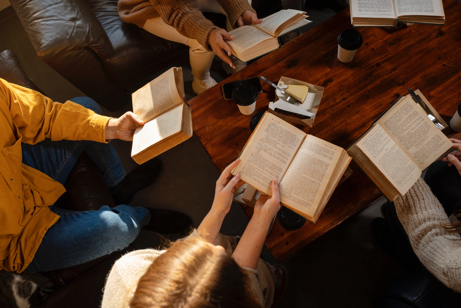 View of 4-5 adults reading books surrounding a coffee table.