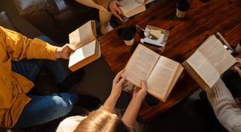 View of 4-5 adults reading books surrounding a coffee table.