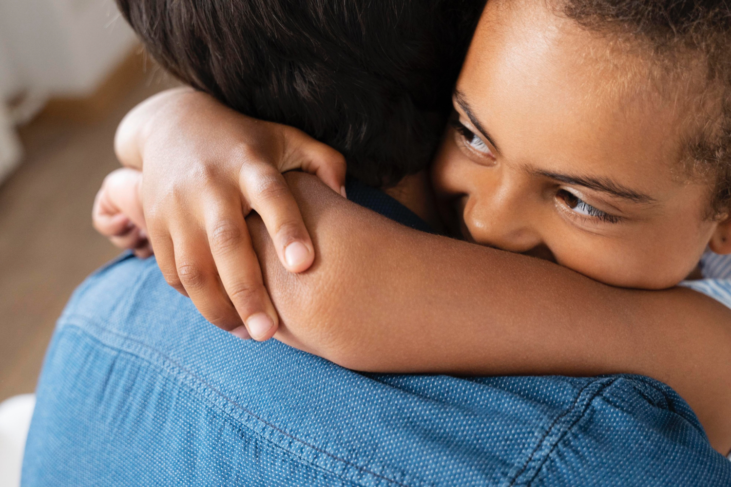 Closeup of kid hugging adult, wearing a denim shirt. Kid is smiling. 