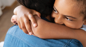 Closeup of kid hugging adult, wearing a denim shirt. Kid is smiling. 