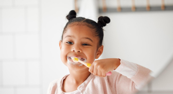 Little girl wearing pink shirt brushing her teeth with toothpaste all over her face. 