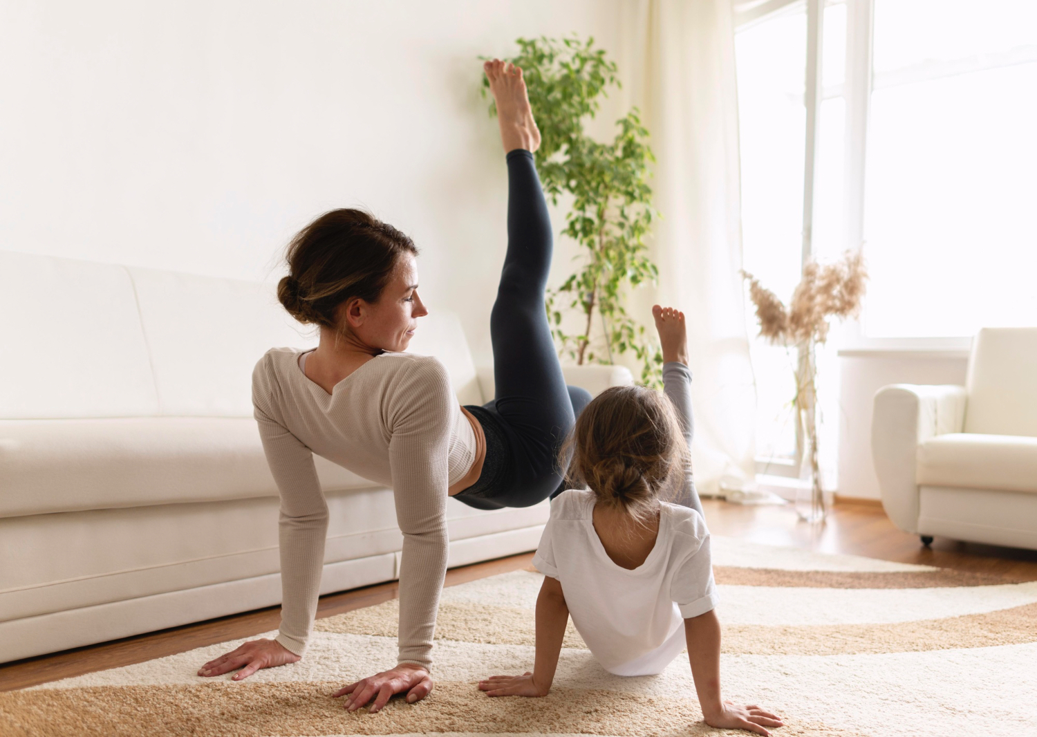 Adult female and toddler girl doing yoga in bright living room setting. 