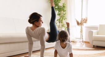 Adult female and toddler girl doing yoga in bright living room setting. 