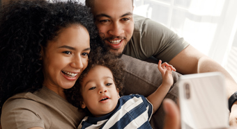 Adult female and male smile while taking a selfie with toddler in their lap wearing blue striped shirt.