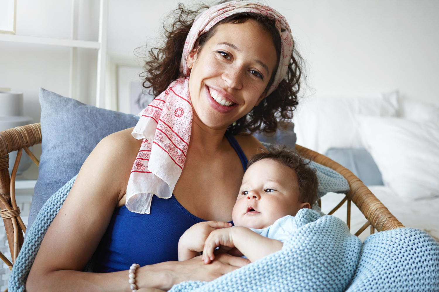 Adult female smiling at camera, holding a toddler in her lap while sitting in a cozy home setting. 