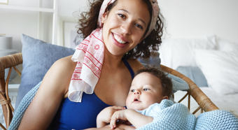Adult female smiling at camera, holding a toddler in her lap while sitting in a cozy home setting. 