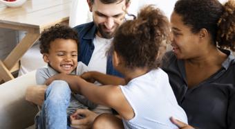 Two adults and two young children tickling each other on a couch.