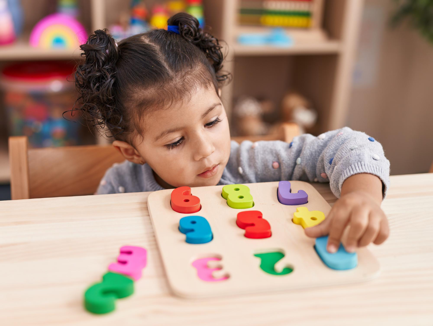 little giril in colorful classroom setting plays with a colorful numbers toy