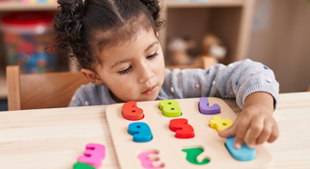 little giril in colorful classroom setting plays with a colorful numbers toy