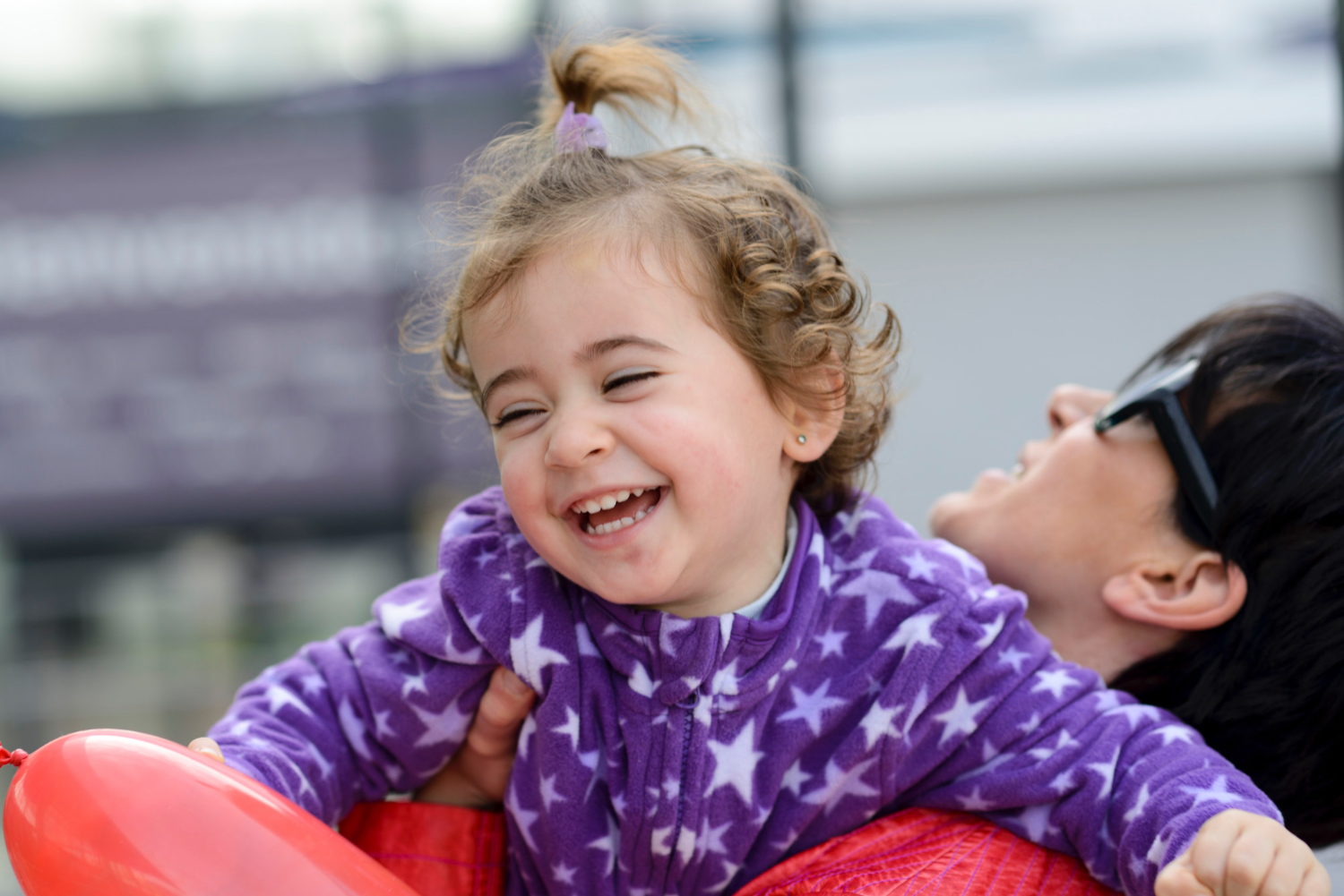 Young girl being held by an adult smiles while wearing a purple fleece jacked with stars on it.