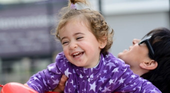 Young girl being held by an adult smiles while wearing a purple fleece jacked with stars on it.