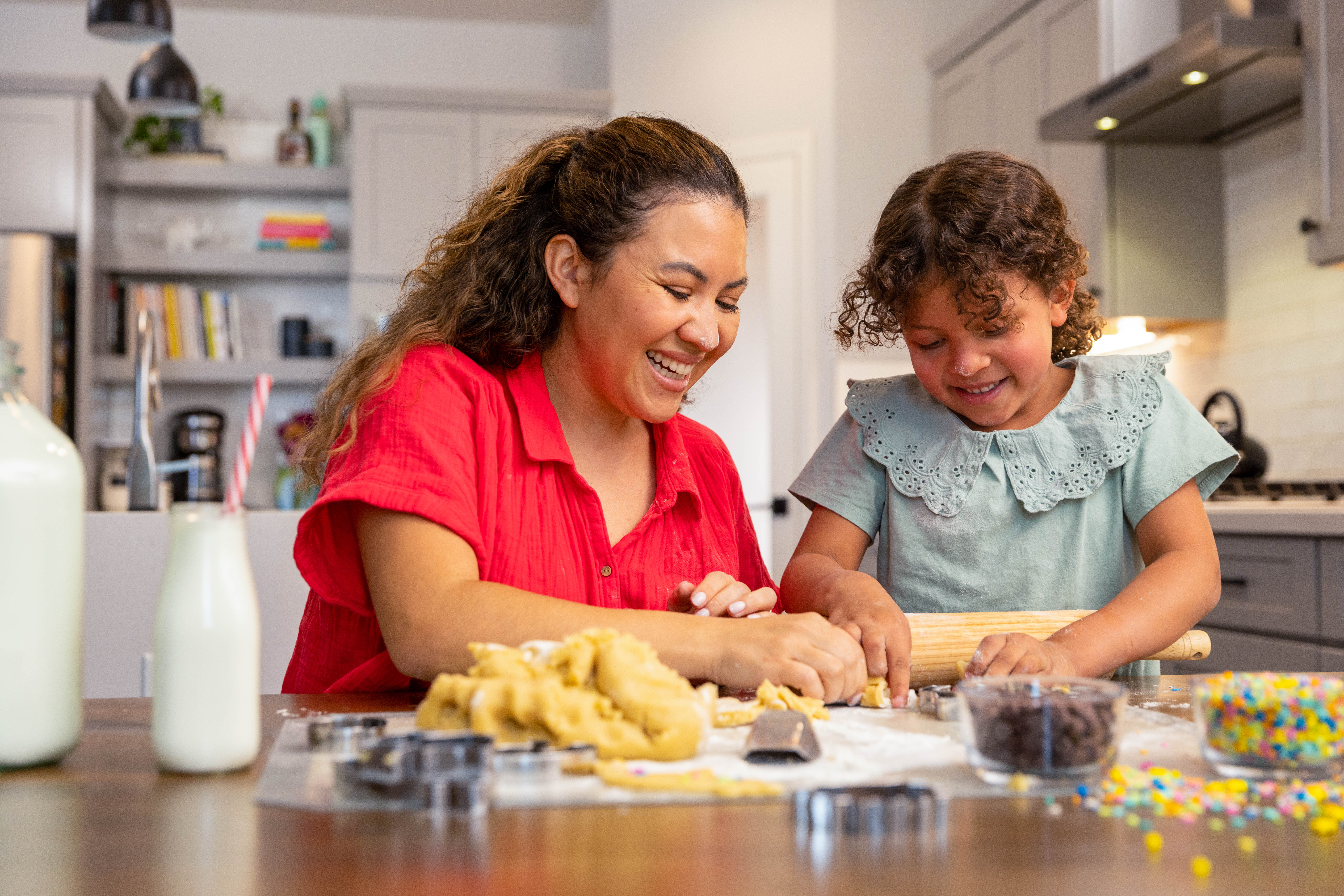 Little girl and adult female sit in kitchen laughing and making holiday sugar cookies. 