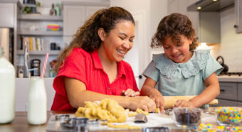 Little girl and adult female sit in kitchen laughing and making holiday sugar cookies. 