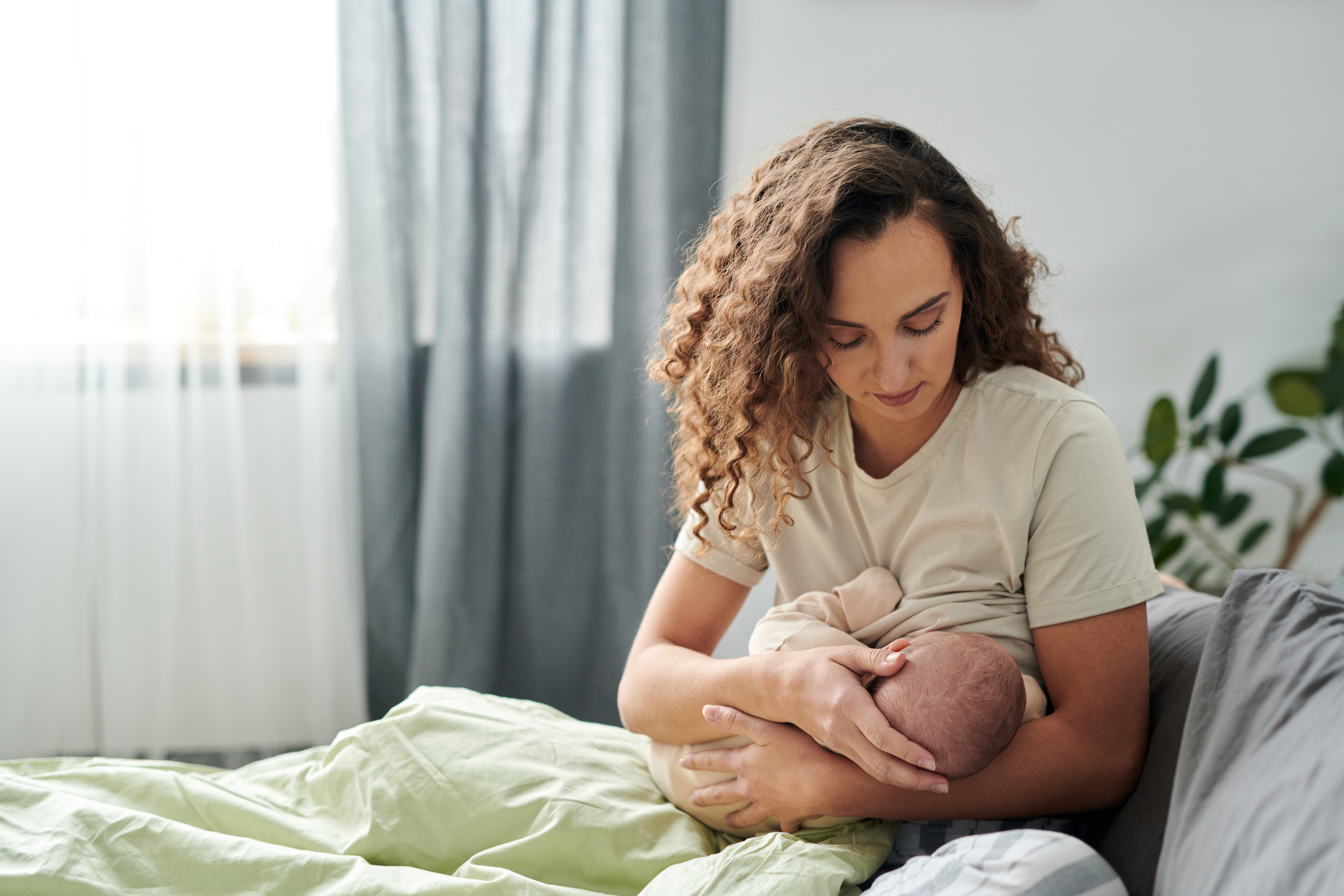 Women in a cozy room setting sitting in bed while breastfeeding.