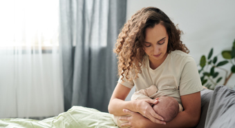 Women in a cozy room setting sitting in bed while breastfeeding.