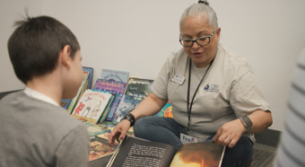 Women and kid sitting on floor while women reads a story to the child. 