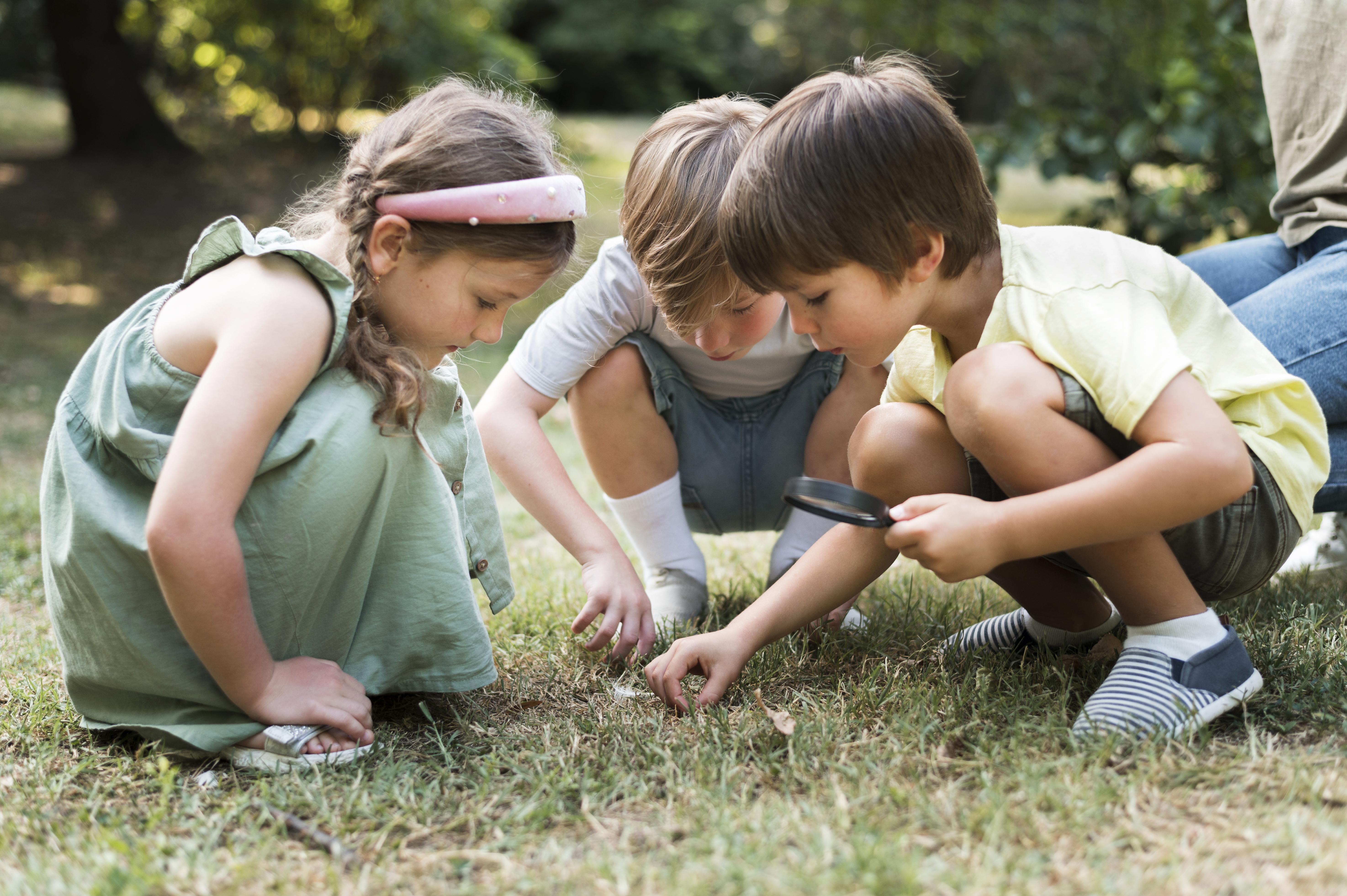 Three young children looking in the grass for bugs. 