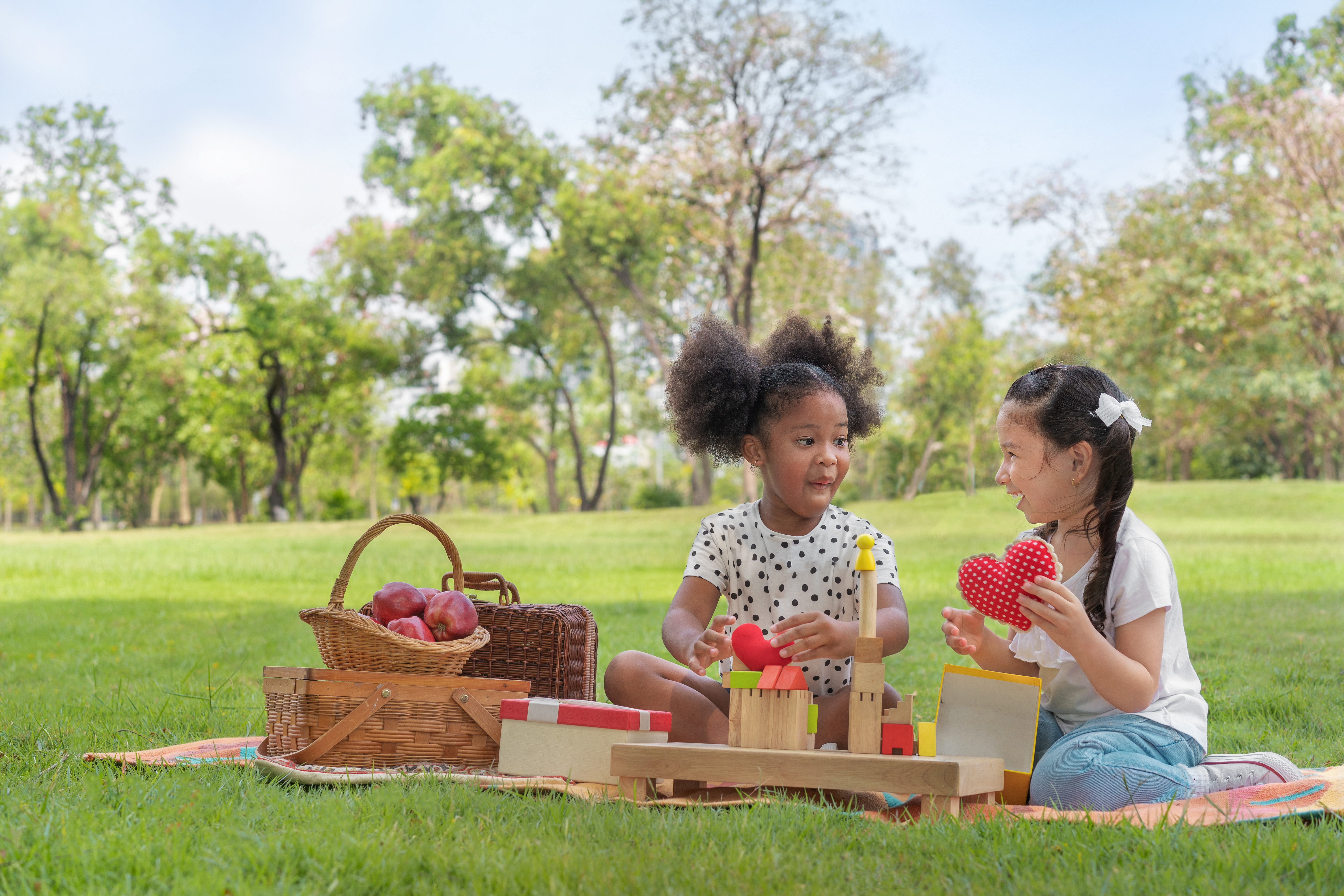 Two young girls having a picnic in a park setting on the green grass, picnic basket with apples