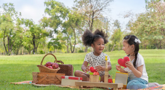 Two young girls having a picnic in a park setting on the green grass, picnic basket with apples