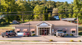 Exterior shot of rural building, green trees in background, 3 cars parked in front of the single story building. 
