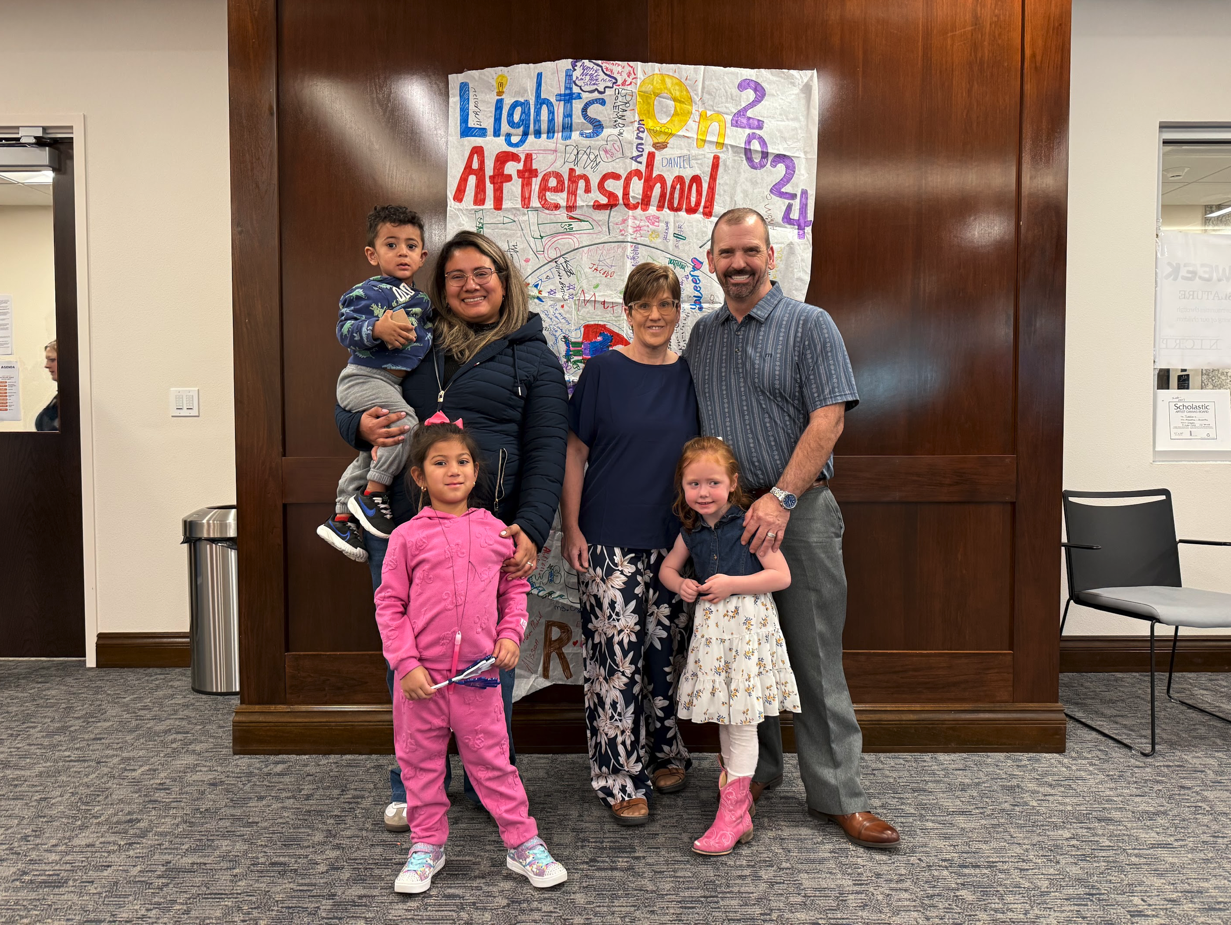 Three little children with two adult females and one male smiling at camera during Children's Week session.