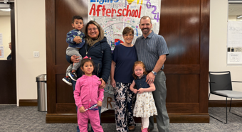 Three little children with two adult females and one male smiling at camera during Children's Week session.