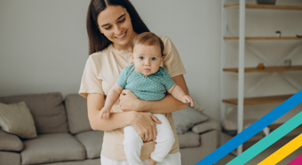 Adult female holding toddler in her arms looking at the toddler and smiling. In a comfy house setting. 