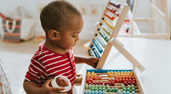 Toddler playing with rainbow children's games, wearing red stripped shirt and holding a toy football. 