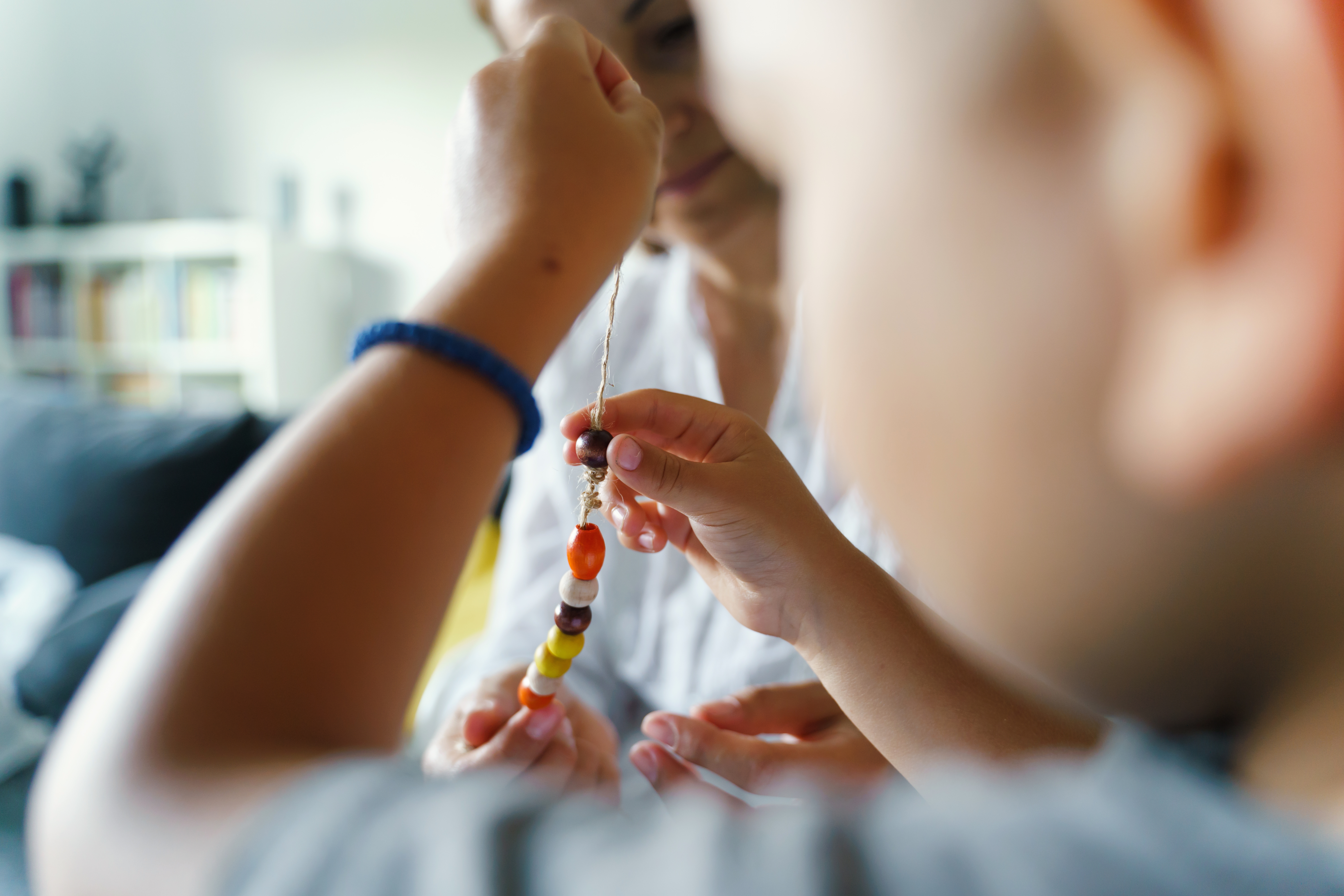 Close up visual of toddler playing with beads on a string, while parental figure watches and helps 