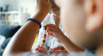 Close up visual of toddler playing with beads on a string, while parental figure watches and helps 