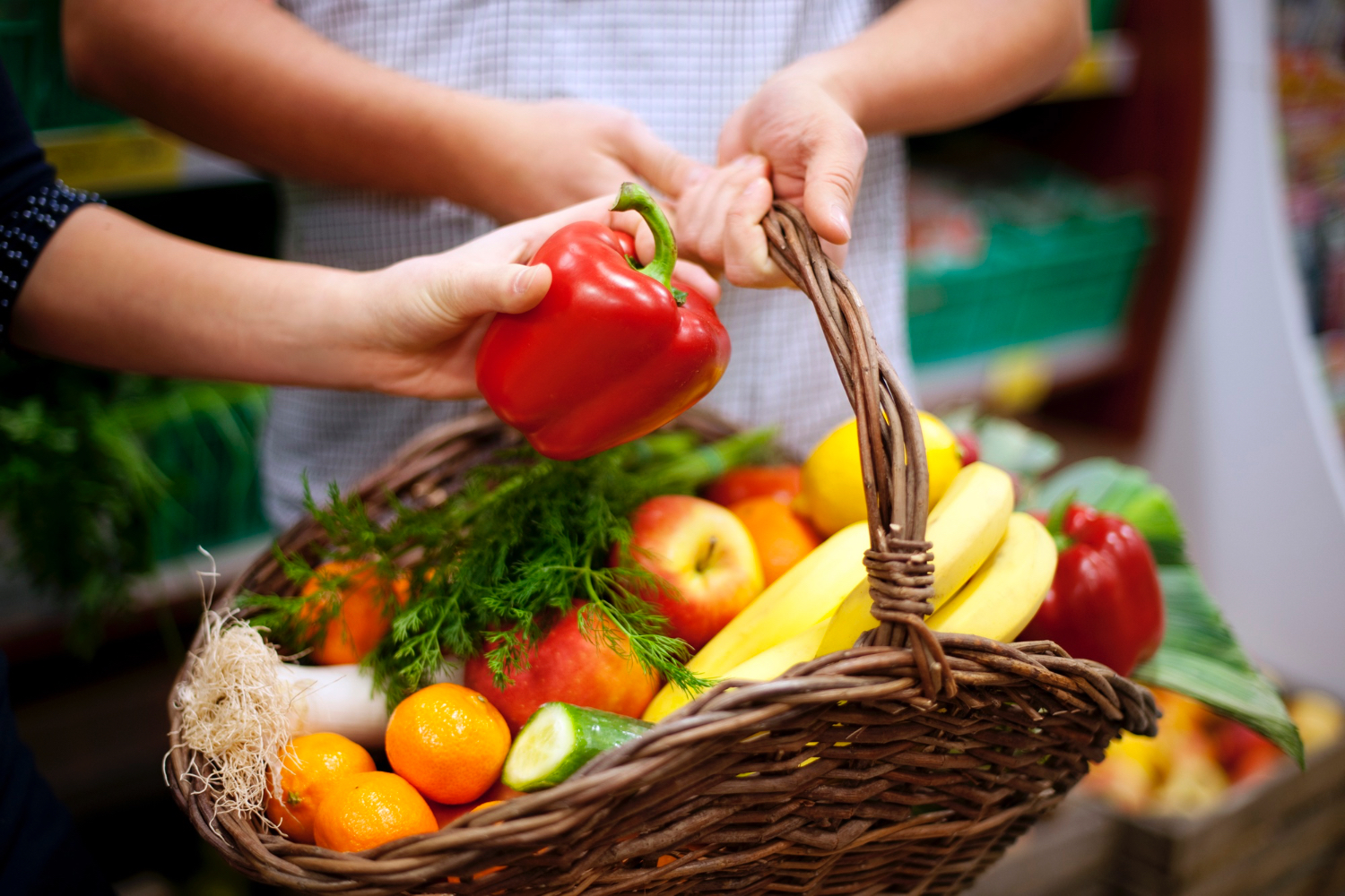 Closeup of hand reaching into a basket filled with various fruits and vegetables. 