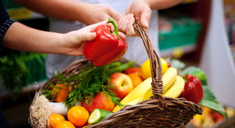 Closeup of hand reaching into a basket filled with various fruits and vegetables. 