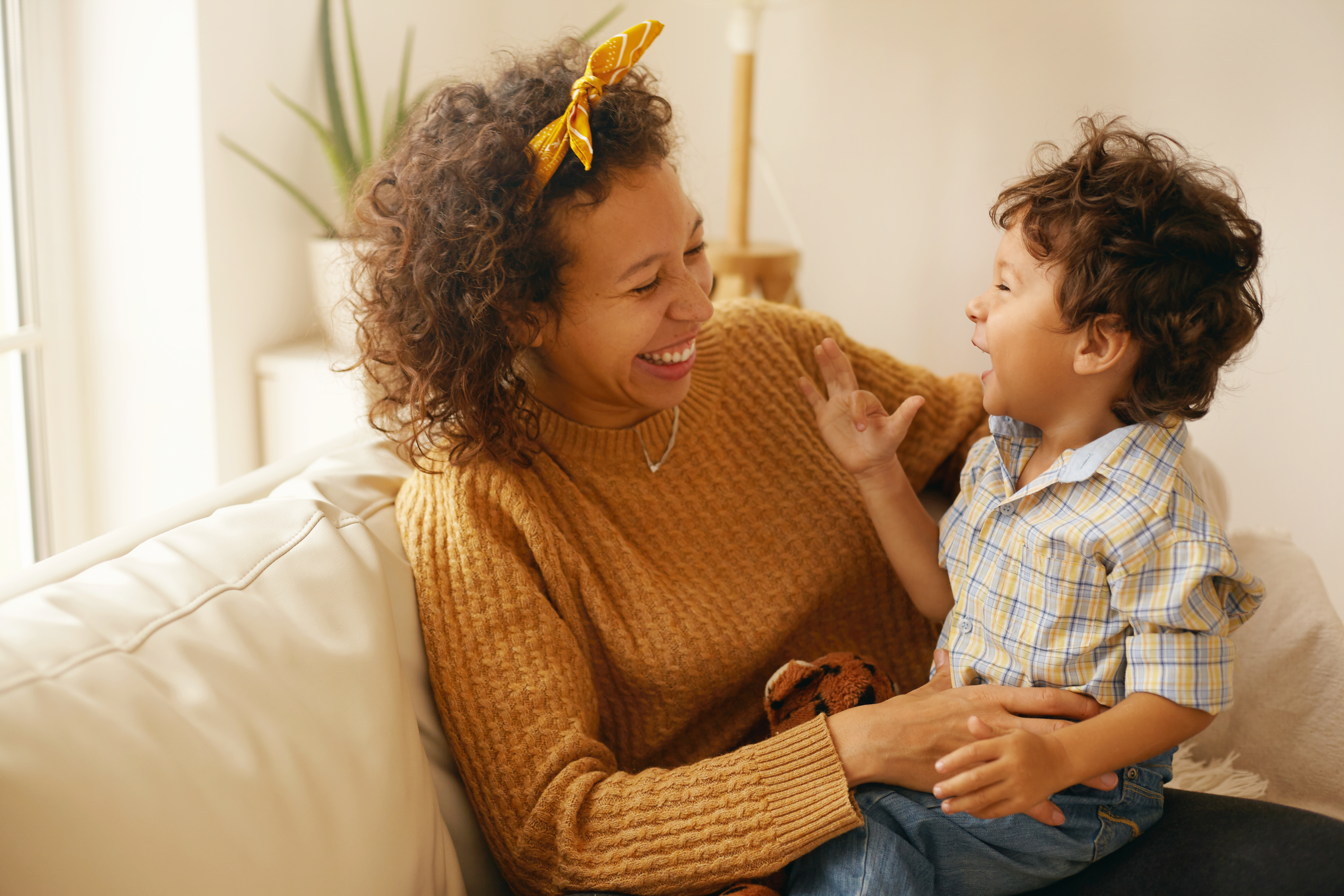 Adult female wearing orange sweater laughs and smiles with the toddler sitting in her lap.