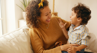 Adult female wearing orange sweater laughs and smiles with the toddler sitting in her lap.