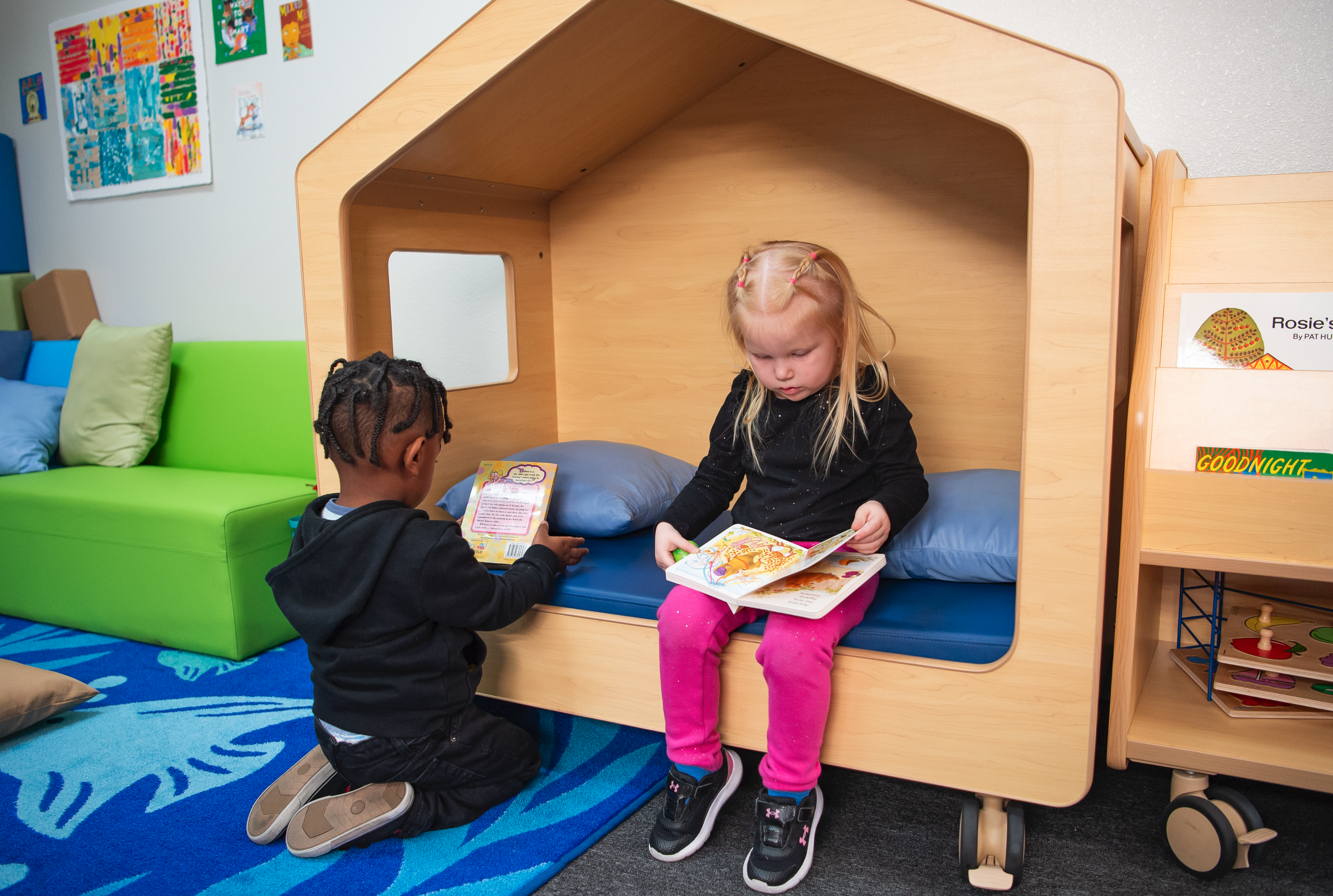 Two small children sitting next to each other while reading children's books in a child's playhouse. 