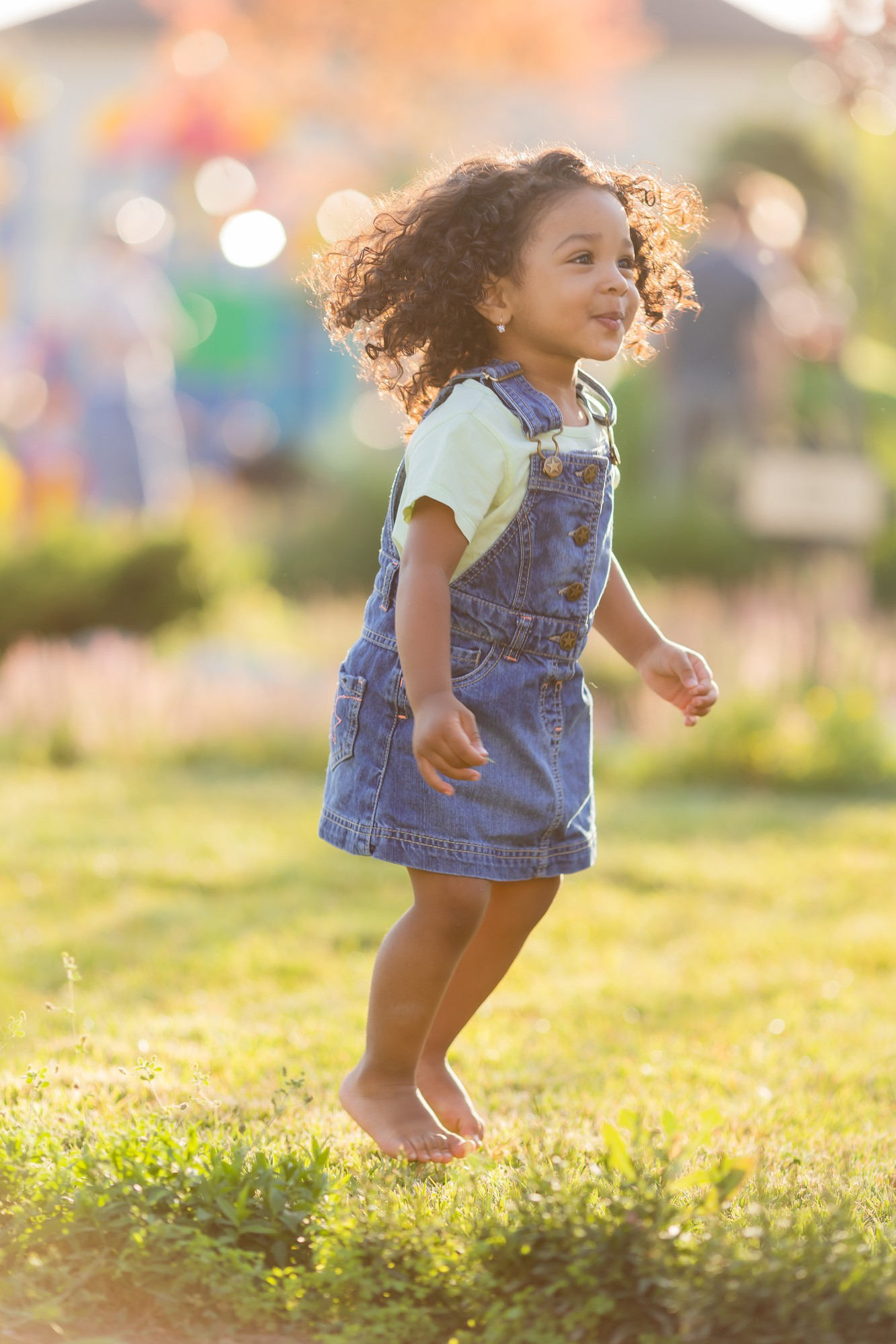 Smiling toddler in a bright outdoor setting, playing on the grass. 