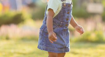 Smiling toddler in a bright outdoor setting, playing on the grass. 