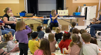 Children in a classroom being read a book by the teacher.