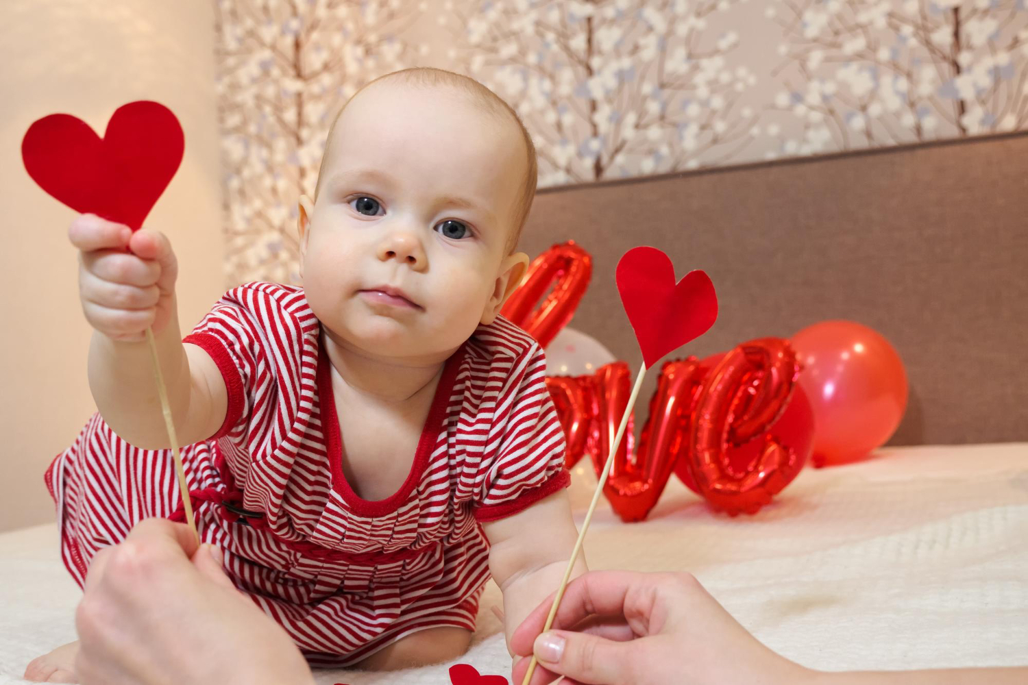 Baby looking at camera wearing red and holding paper heart cutouts. 